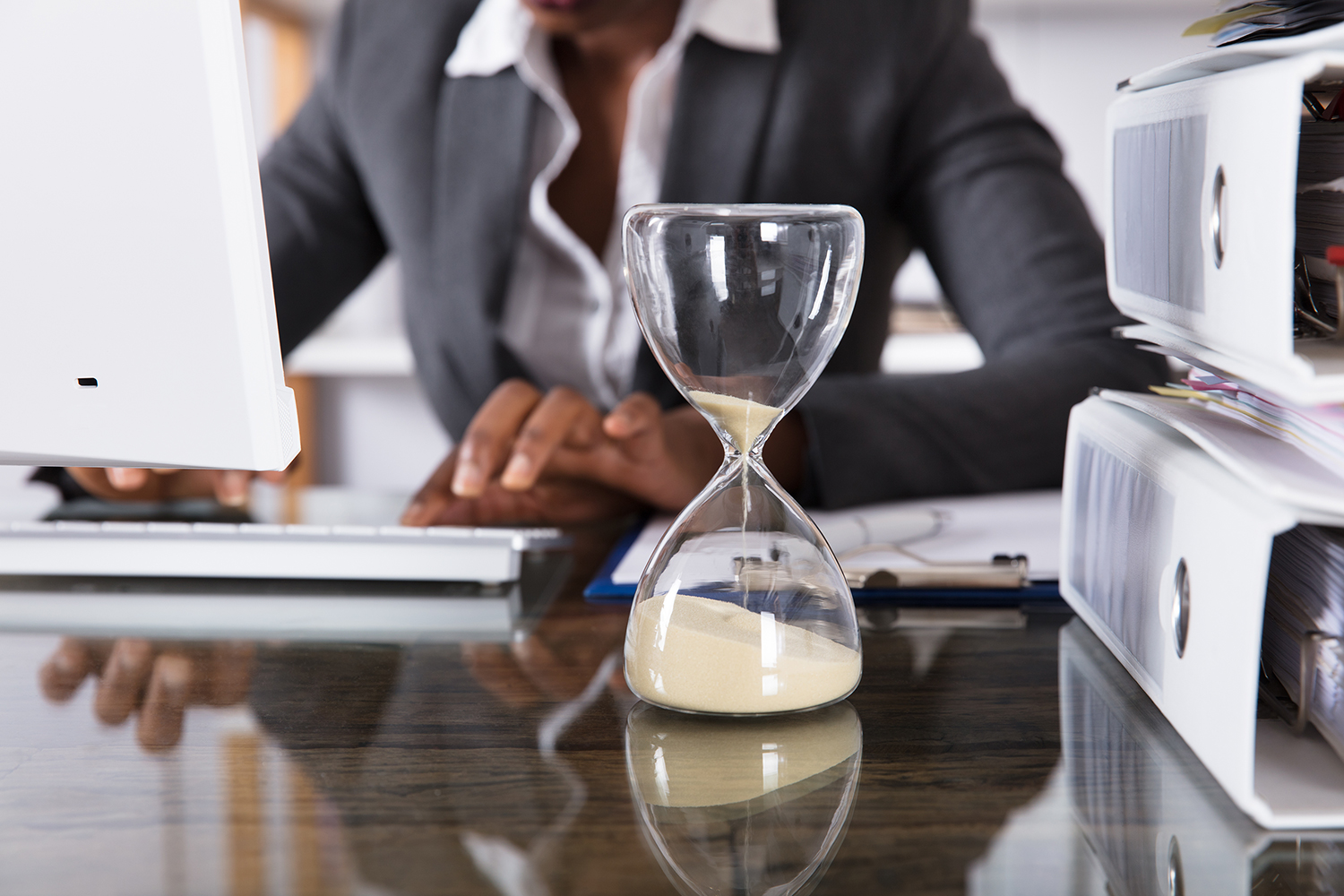 Mujer en su oficina, computadora, reloj de arena y archivos sobre el escritorio