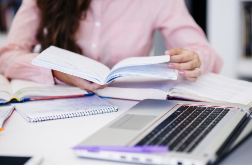 Mujer leyendo un cuaderno al frente de ella una computadora portátil